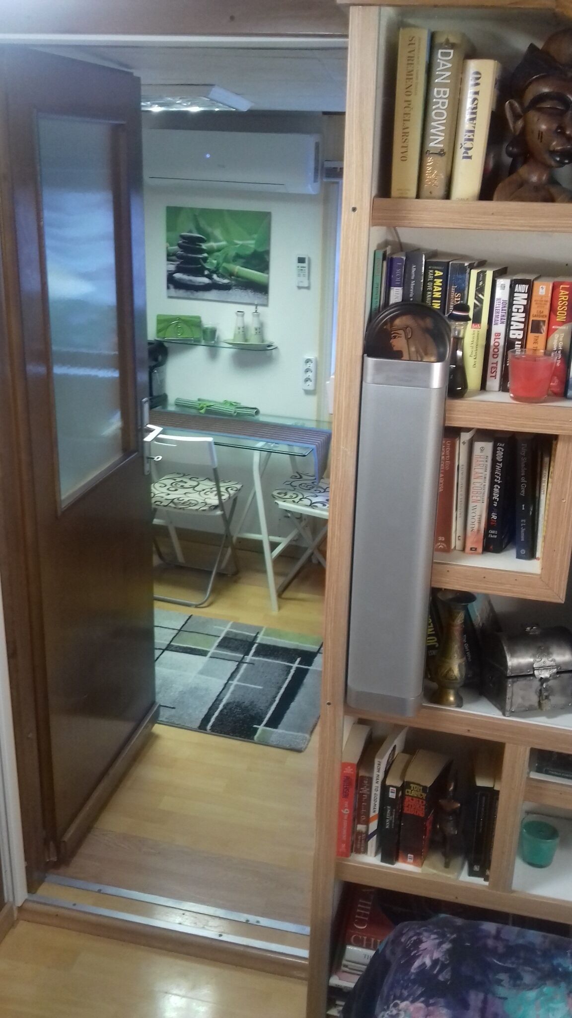 Keittiö, jossa on ruokapöytä ja -tuolit, jääkaappi sekä kirjahylly, jossa on erilaisia kirjoja ja koriste-esine.