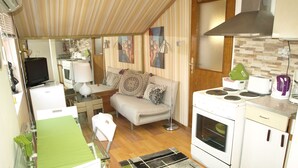 A compact kitchen with a stove, microwave, and small refrigerator. There is a dining table with chairs and a green tablecloth. A sofa and a floor lamp are in the living area. - STUDIO GREEN   near city center, free parking, wifi, at banks of river Sava (Zagreb)