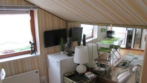 A compact room with a kitchenette, a small fridge, a desk with a lamp, a chair, and a television on the wall. - STUDIO GREEN   near city center, free parking, wifi, at banks of river Sava (Zagreb)