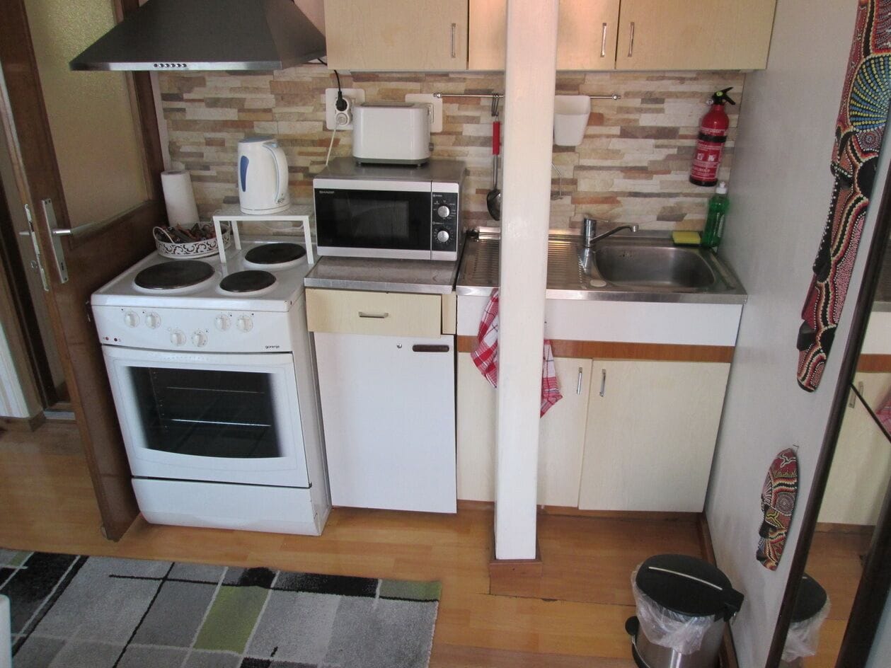 Cocina compacta con estufa, microondas y refrigerador pequeño. Hay un lavamanos y un extintor de incendios en la pared.