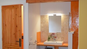 Un bany amb una porta de fusta, un lavabo amb mirall i un sòl de rajola.