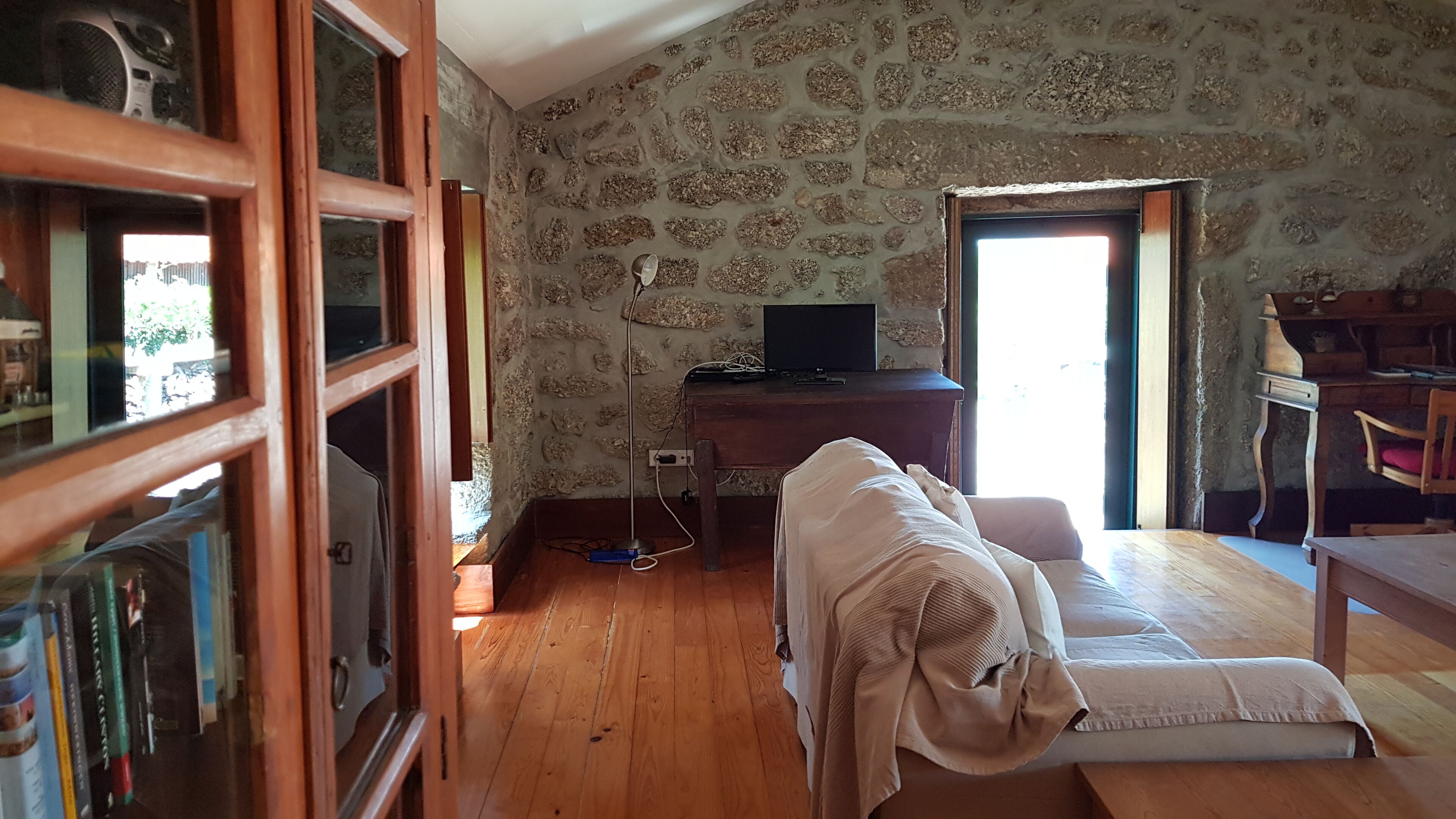A room with a stone wall, wooden floor, a desk with a computer, a chair, and a bookshelf.