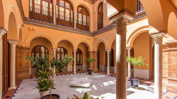 Un cortile con archi, colonne e piante in vaso.