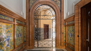 Un elegante corridoio con pavimento piastrellato, una porta decorativa con cancello in metallo e pareti ornate da complesse decorazioni in piastrelle.