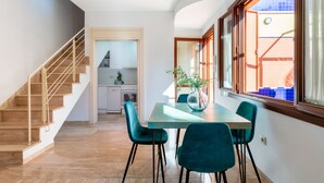 Una cucina moderna con mobili bianchi, un'area pranzo con sedie color verde acqua e una scala con ringhiera in legno.