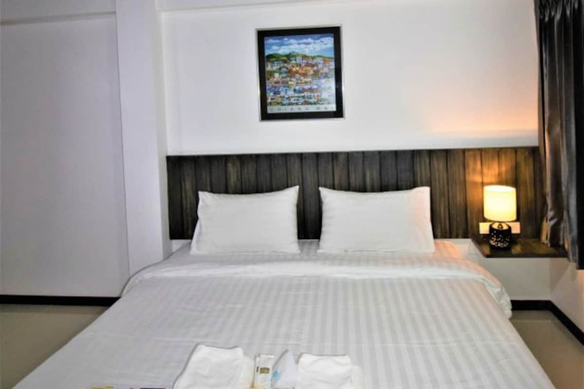 A hotel room with a large bed, a framed picture on the wall, and a bedside lamp.