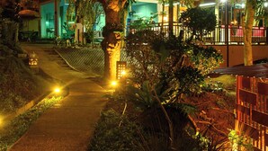 A modern building with a glass facade, surrounded by lush greenery and illuminated by warm lighting. - Thai Modern Resort & Spa (Chalong)