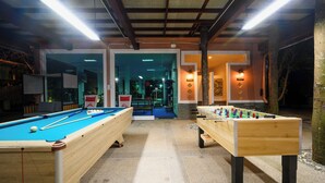 A pool table, foosball table, and a billiards table in a well-lit indoor recreational area with a modern design. - Thai Modern Resort & Spa (Chalong)