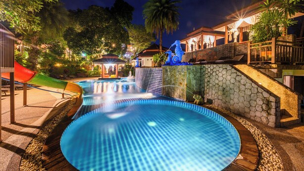 A swimming pool with a slide, surrounded by stone walls and palm trees. - Thai Modern Resort & Spa (Chalong)