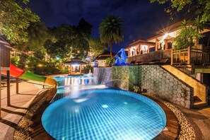 Une piscine avec un toboggan, entourée de murs en pierre et de palmiers.
