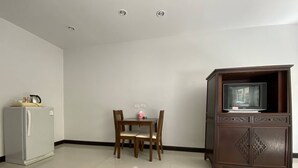 A room with a dining table and chairs, a refrigerator, and a cabinet with a television. - C.A.P. Mansion Hotel (Phuket)