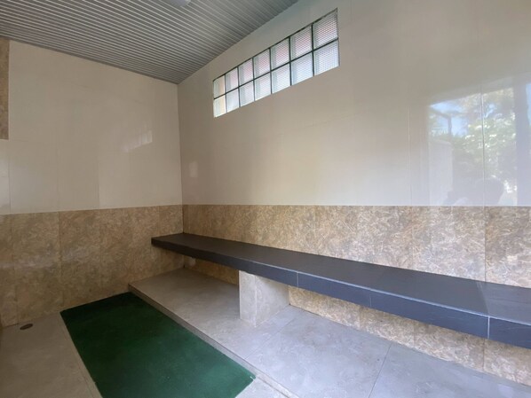 A room with a tiled floor, a green mat, a black bench, and a window with blinds.