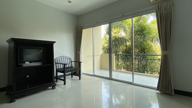 A spacious room with a large sliding glass door leading to a balcony, a television on a stand, and a chair. - C.A.P. Mansion Hotel (Phuket)