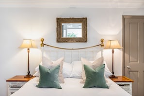 A neatly made bed with two pillows, two bedside lamps, and a mirror on the wall.