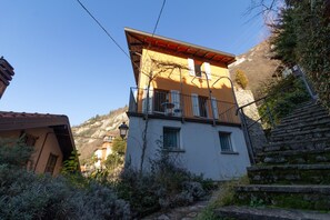 A two-story building with a balcony, surrounded by vegetation and a mountain backdrop.