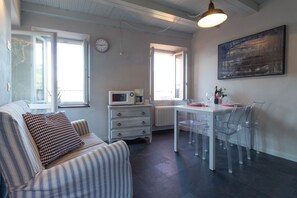A modern living room with a striped sofa, a dining table with chairs, a microwave, and a clock on the wall.