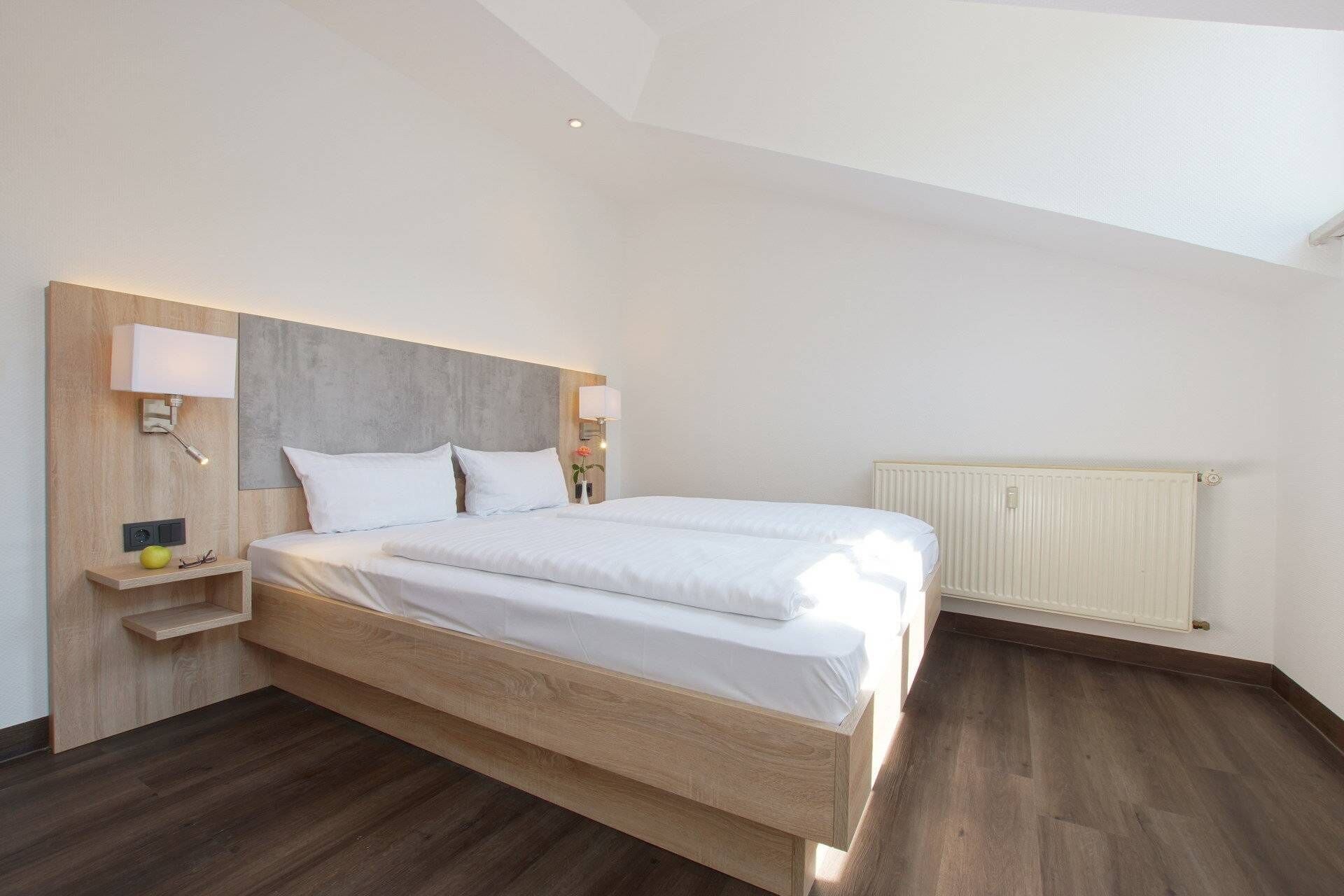 A modern bedroom with a large bed, wooden headboard, bedside lamps, and a radiator.