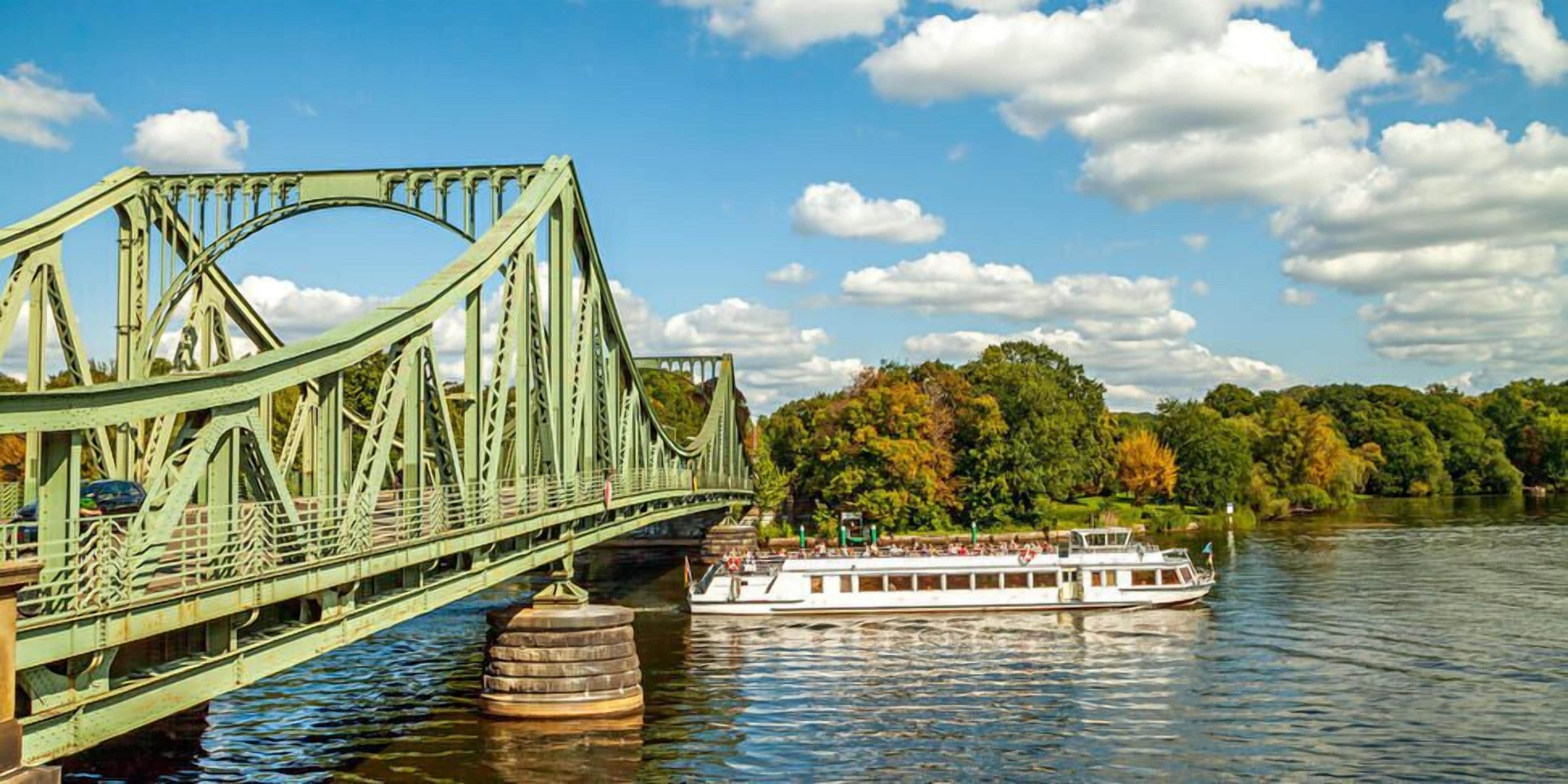 A green steel bridge over a river with a boat on the water.