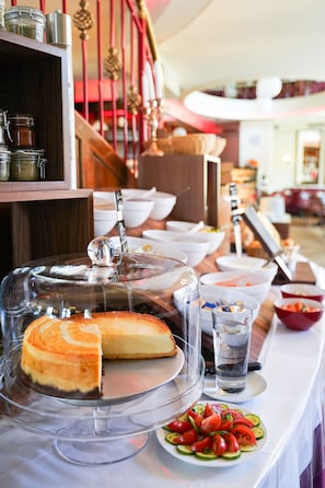 Una mesa de buffet con un pastel de queso, un plato de tomates en rodajas y diferentes fuentes de comida.