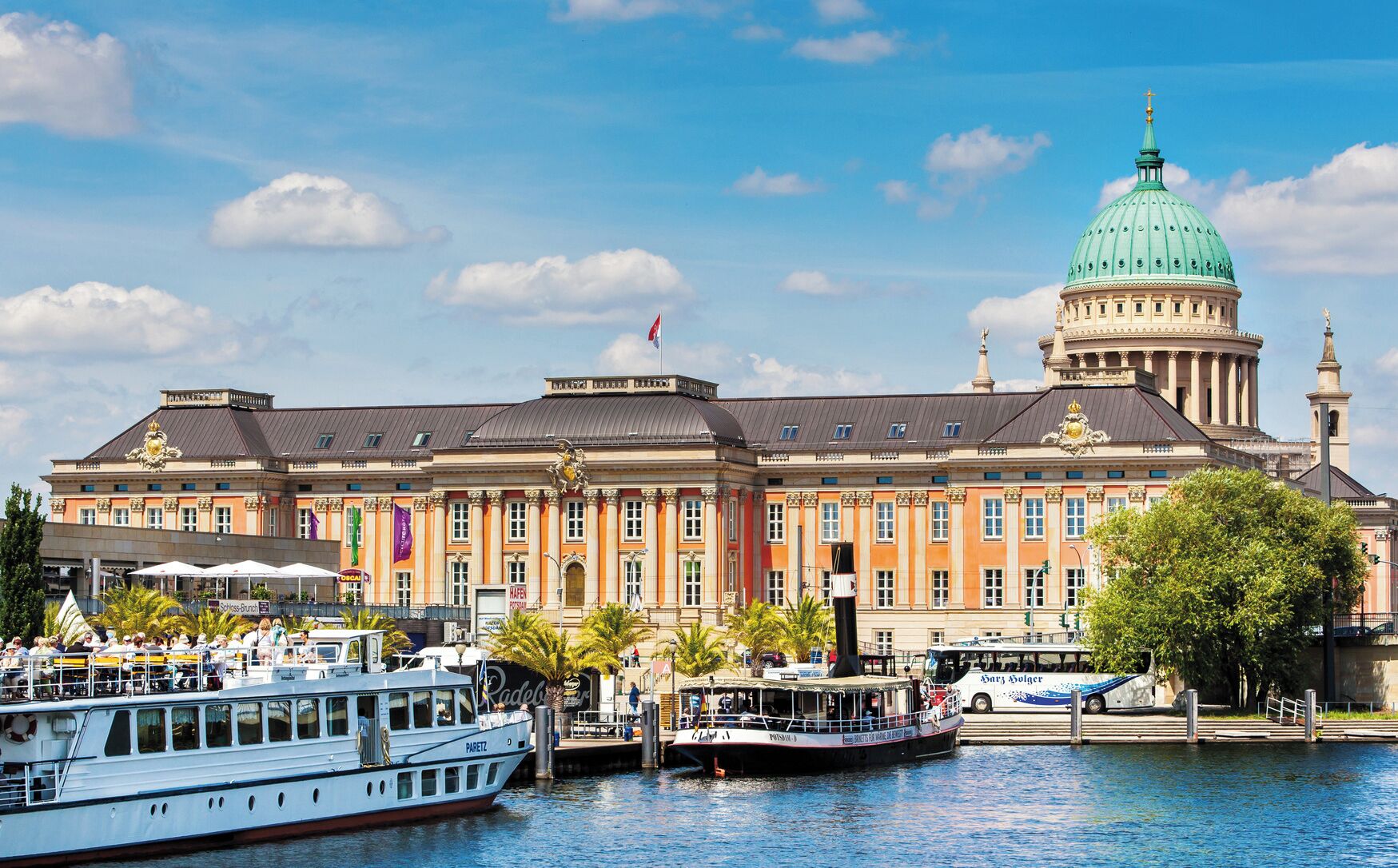 A historic building with a prominent dome and classical architecture, situated by a waterfront with boats docked nearby.