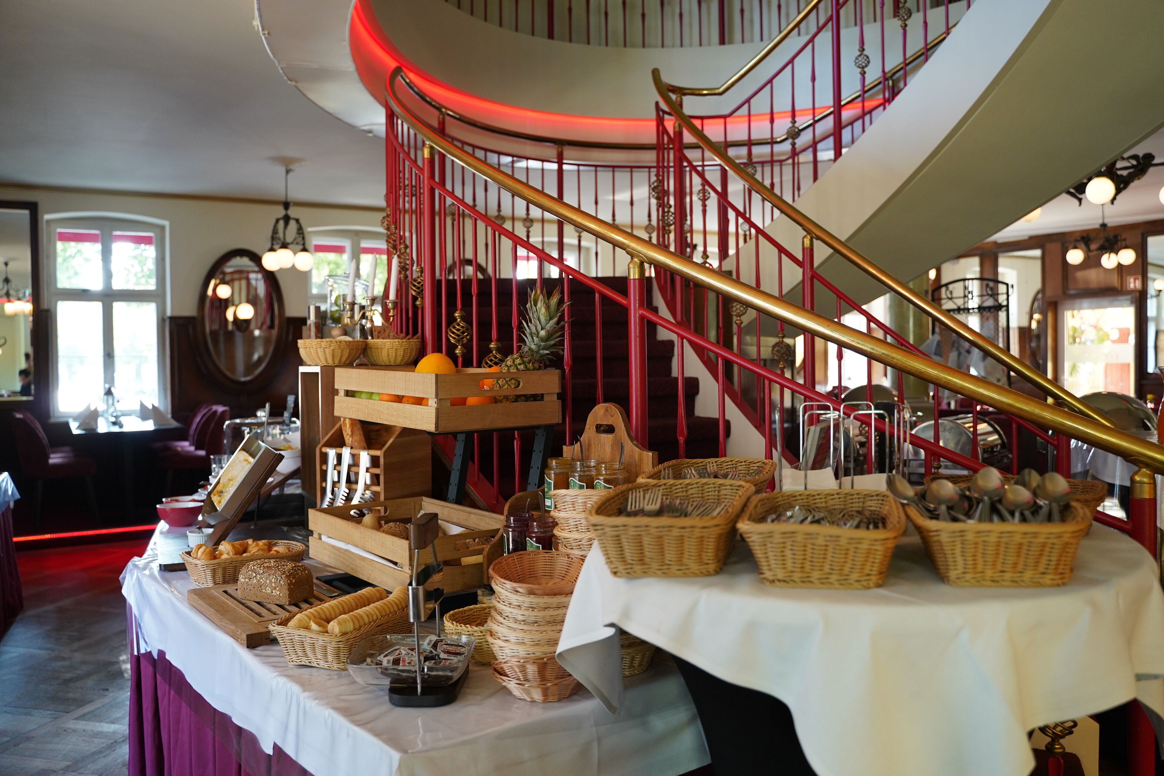 A dining area with a buffet table, wicker baskets, and a red spiral staircase.