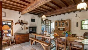 Una cocina rústica con vigas de madera, piso de piedra y una mesa de comedor de madera con bancos.