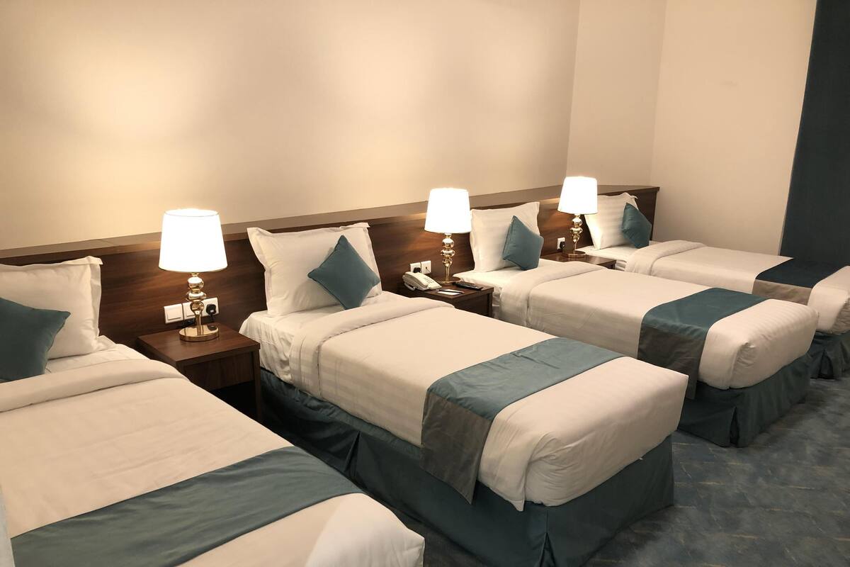 Une chambre d’hôtel avec quatre lits simples, chacun étant équipé d’une table de chevet, d’une lampe et d’un téléphone.