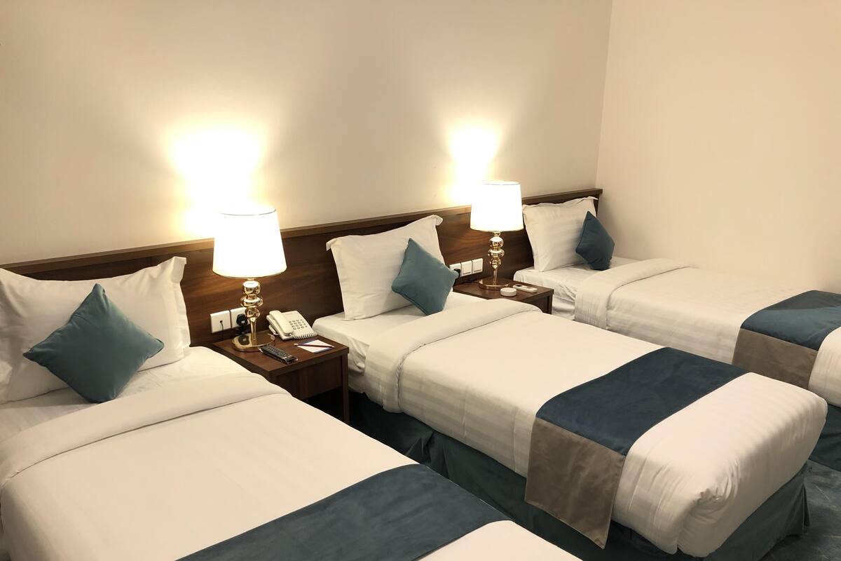 Une chambre d’hôtel avec trois lits simples, chacun étant équipé d’une table de chevet, d’une lampe et d’un téléphone.