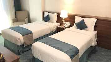 Ein Hotelzimmer mit zwei Betten, einem Nachttisch mit Lampe, einem Telefon und einem Sessel.