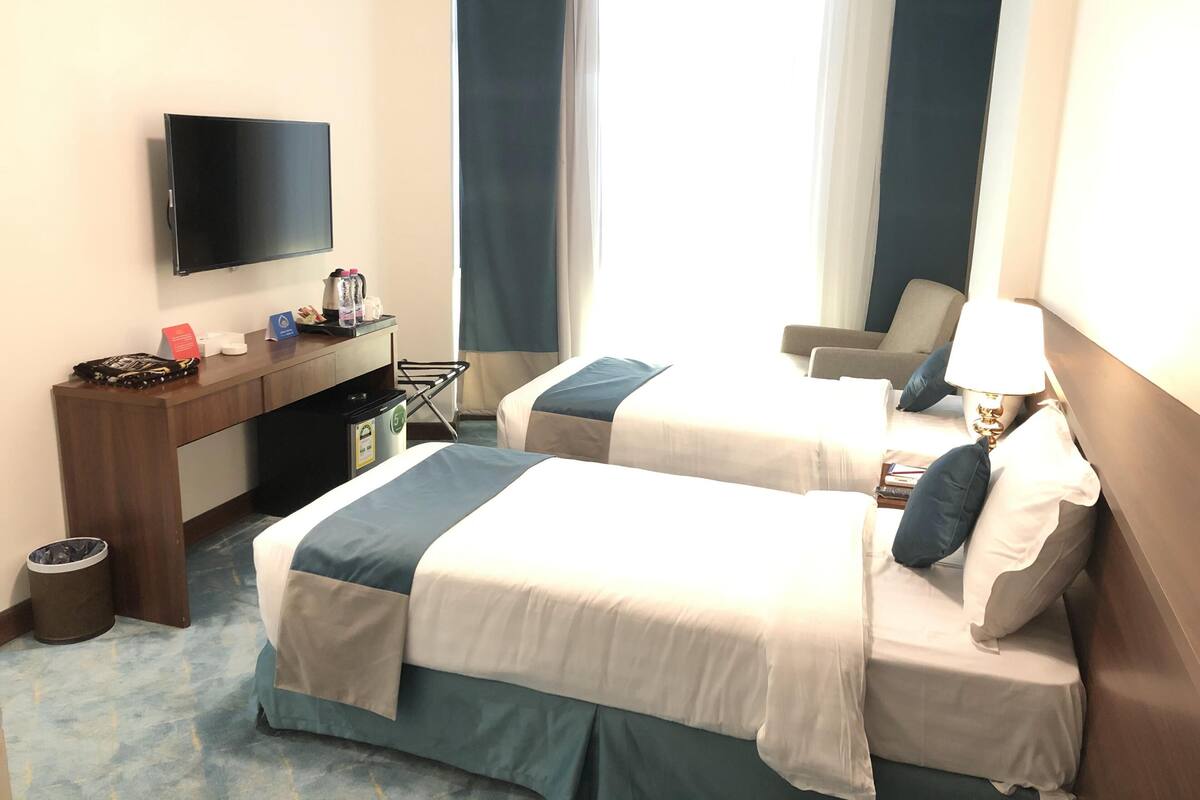 Une chambre d’hôtel avec deux lits, un bureau, une télévision, une chaise et une lampe.