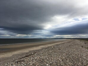 A pebbled beach with a wide view of the ocean under a cloudy sky. - Washington House (Nairn)