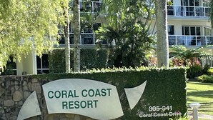 Une enseigne pour le Coral Coast Resort, avec un mur en pierre et de la verdure.