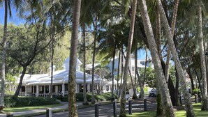 Un hôtel à la façade blanche, entouré d’une végétation luxuriante et de grands arbres.