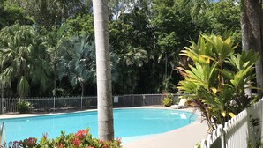 Une piscine entourée d’une végétation luxuriante et délimitée par une clôture blanche.