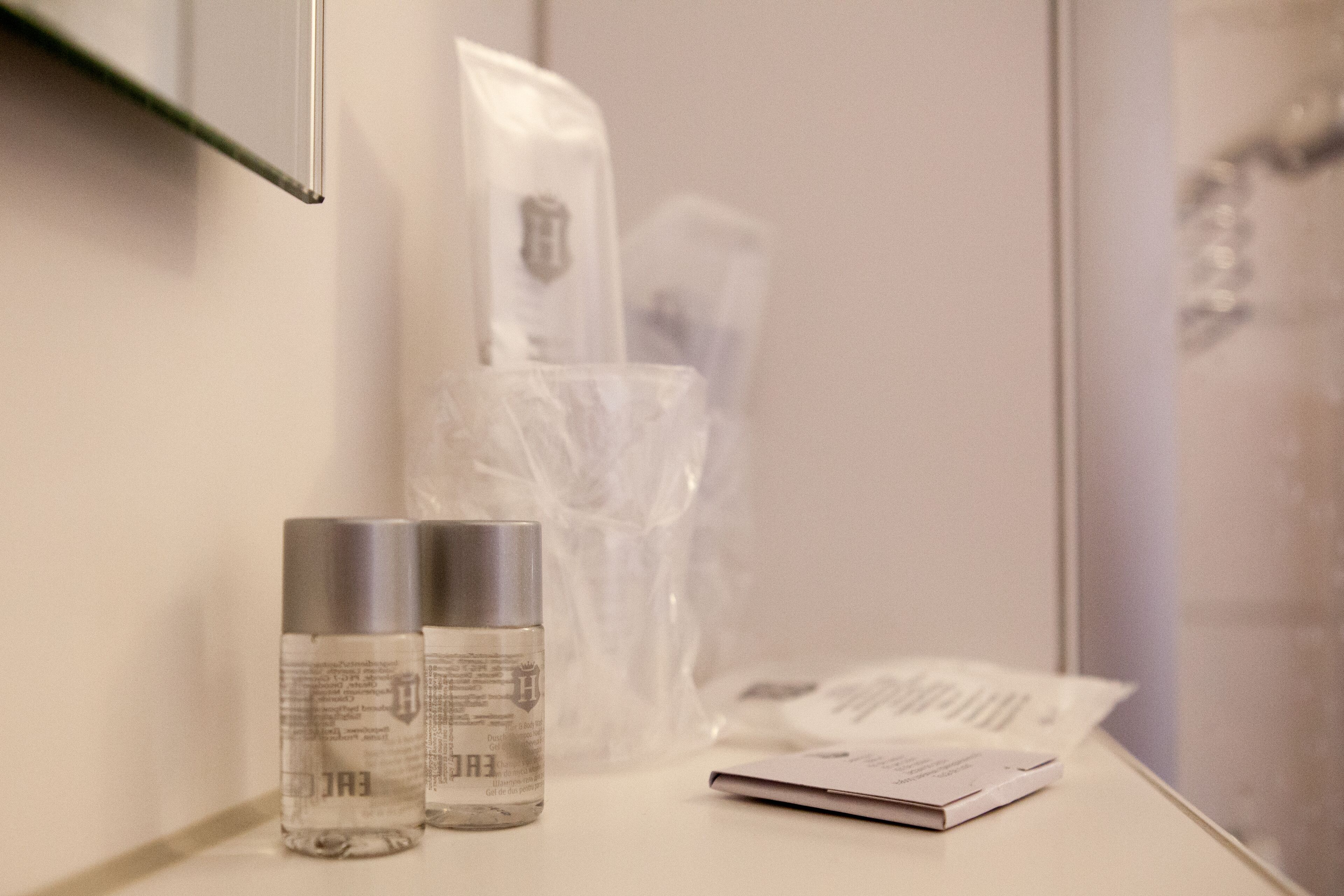 Un baño con un espejo, dos botellas de champú, una bolsa de plástico y una revista en la encimera.