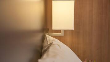 A wall-mounted light fixture on a wooden wall, a white pillow, and a small vase with flowers.