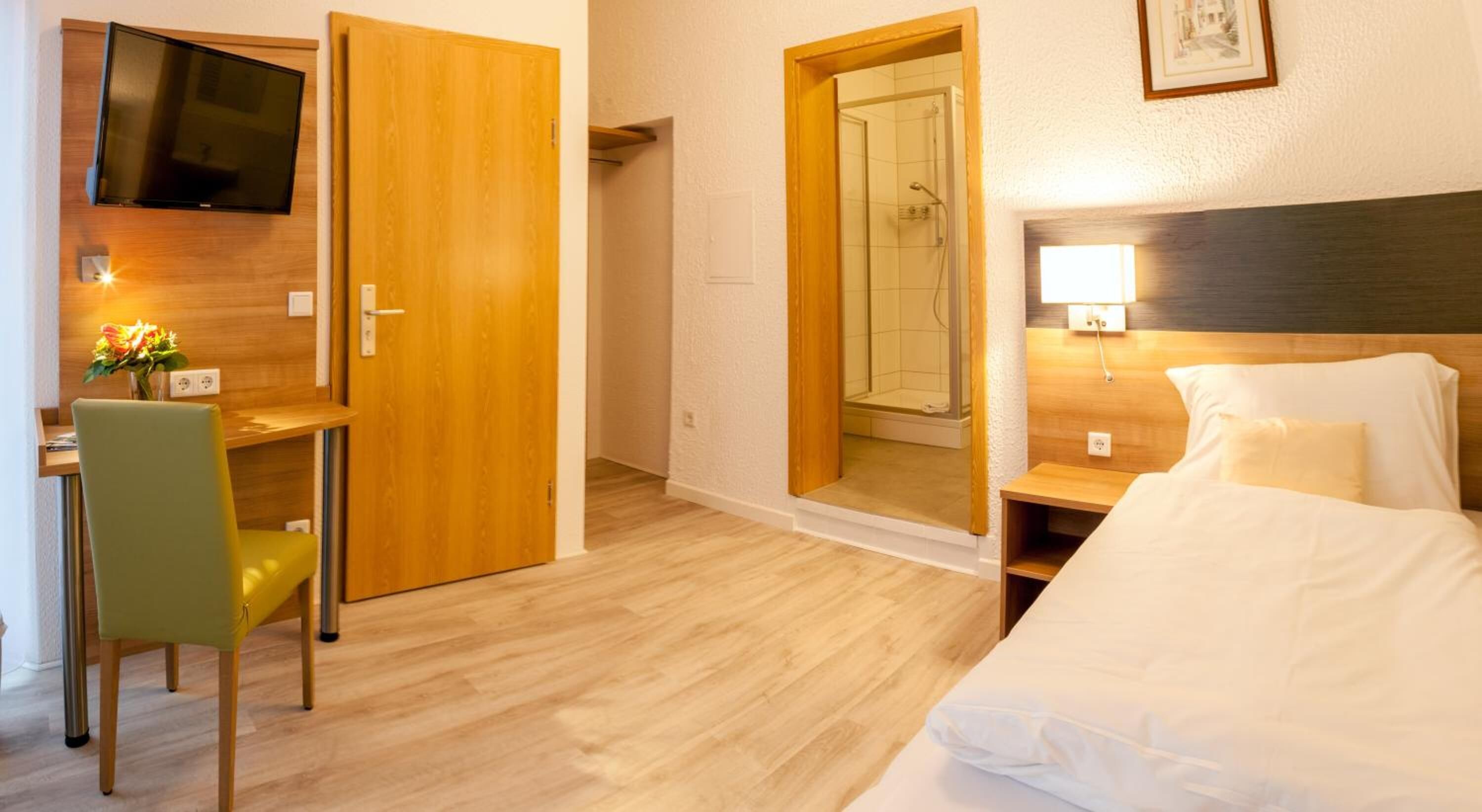 Une chambre d’hôtel comprenant un lit, un bureau avec une chaise, un téléviseur fixé au mur et un espace douche.