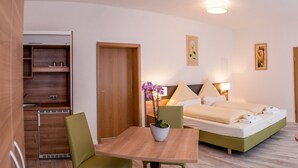 A hotel room with a bed, bedside tables, a small table with chairs, a potted plant, and a window with curtains. - Pension EulenNest (Laubach)