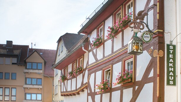 A traditional half-timbered building with a sign for "Steakhaus" and flower boxes on the windows. - Pension EulenNest (Laubach)