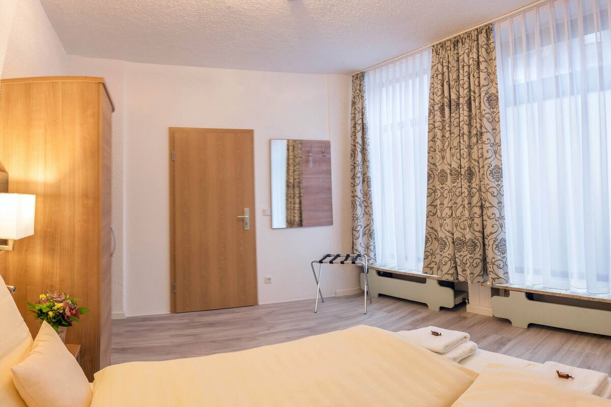 A hotel room with a bed, a desk, a chair, a TV, and a window with curtains.