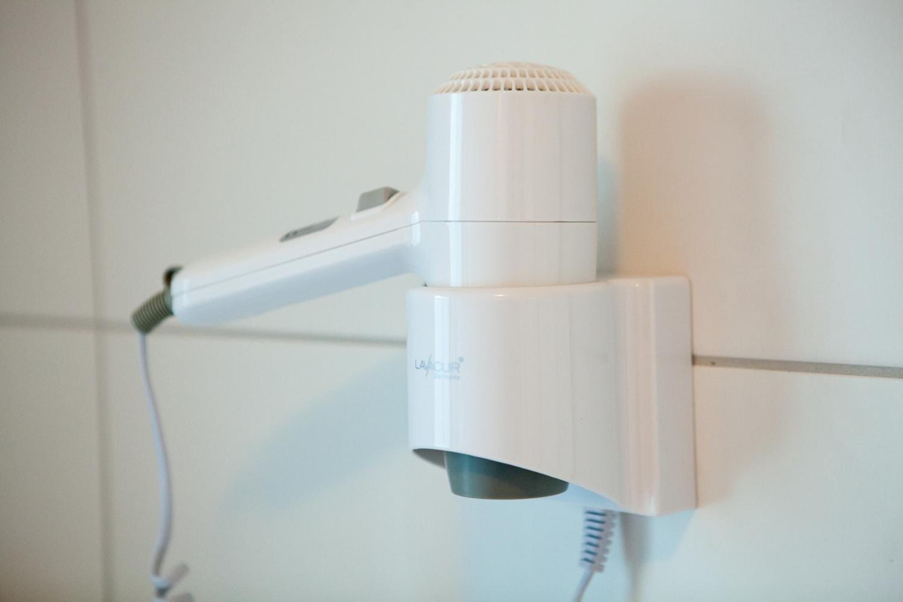 A white hair dryer mounted on a wall with a cord.