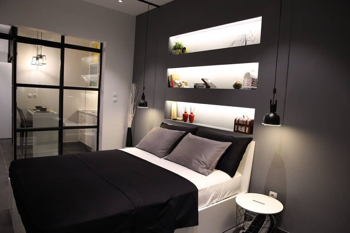 A modern bedroom with a bed, bedside tables, and illuminated shelves displaying various items.