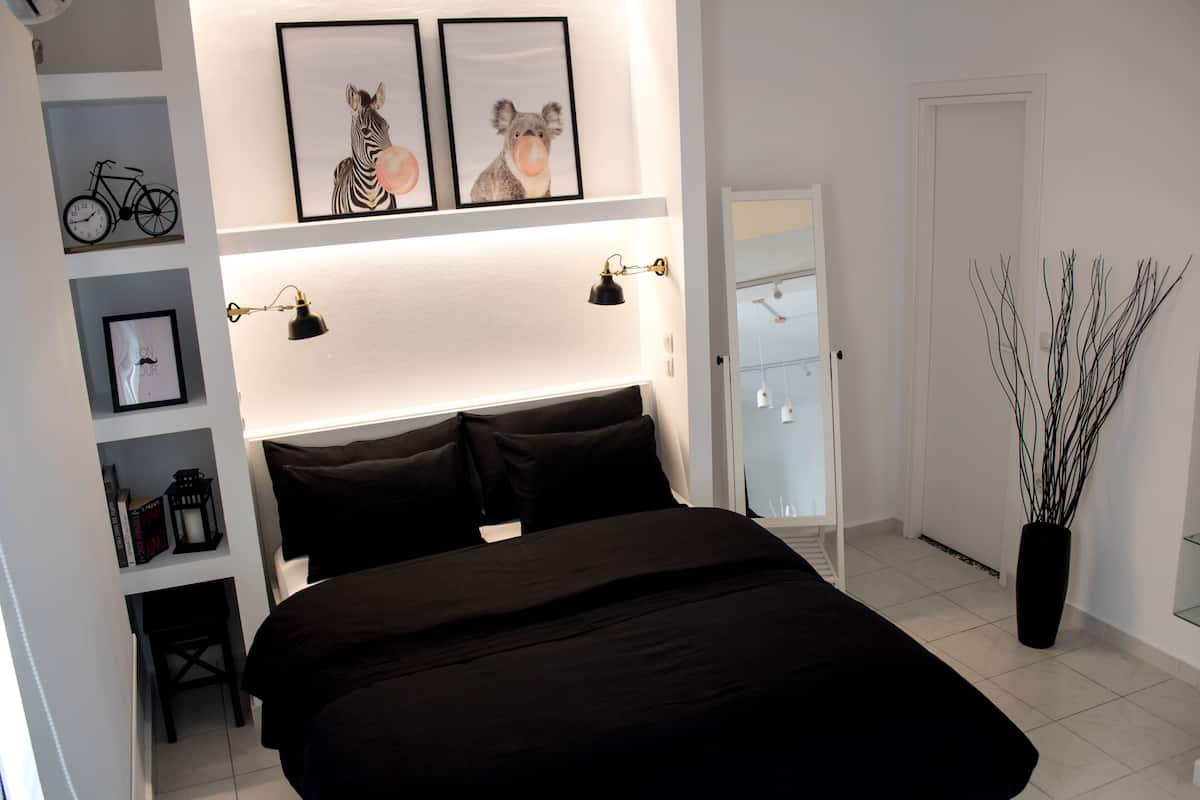 A bedroom with a large bed, a nightstand, a bookshelf with books and a bicycle, and wall-mounted artwork.