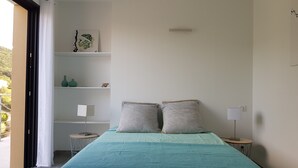 A bedroom with a bed, two pillows, a nightstand, a lamp, and a shelf with decorative items. - Exceptional Villa with Ocean Views in Campomoro, Sleeps 6, Near the Beach (BELVEDERE-CAMPOMORO)