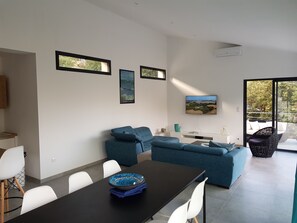 Una sala de estar moderna con comedor, que incluye un conjunto de sofás, una mesa de comedor con sillas y un televisor de pantalla plana montado en la pared.
