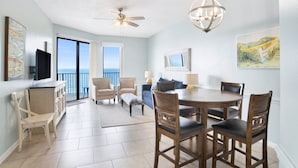 A spacious dining area with a round table and chairs, a ceiling fan, and a chandelier. - Beachfront 2BR @ Phoenix V • Sleeps 8 • Balcony Views, Pools, Indoor Pool & Pirate Splash Pad (Orange Beach)