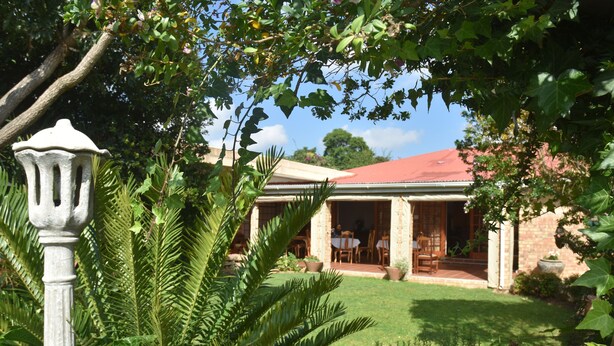 A building with a red roof, surrounded by lush greenery and a well-maintained lawn. - Siesta B&B (Abaqulusi)