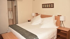 A neatly made bed with a gray throw blanket, wooden headboard, bedside tables with lamps, and a framed picture on the wall. - Siesta B&B (Abaqulusi)