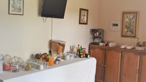 A breakfast buffet setup with a variety of food and drink options, a coffee machine, and a television mounted on the wall. - Siesta B&B (Abaqulusi)