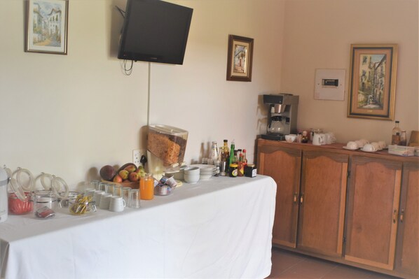 A breakfast buffet setup with a variety of food and drink options, a coffee machine, and a television mounted on the wall. - Siesta B&B (Abaqulusi)